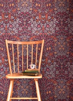 a wooden chair sitting in front of a wall with a floral design on it's back