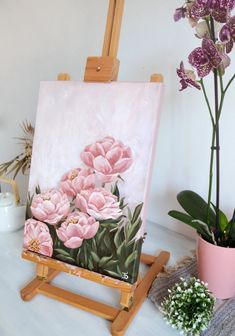 an easel with flowers painted on it next to a potted plant