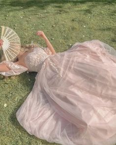 a woman in a pink dress laying on the grass with an umbrella over her head