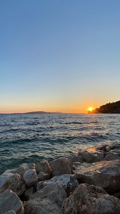 the sun is setting over the water and rocks