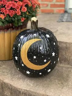 a painted pumpkin with the moon and stars on it sitting next to potted flowers