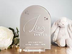 a white bunny sitting on top of a wooden table next to a silver plaque with the name sanitos