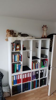 a book shelf filled with lots of books on top of a hard wood floor next to a white wall