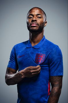 a man wearing a blue shirt and holding a red ball in his right hand while standing against a gray background