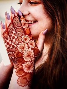 a woman holding her hands up to her face with hendi tattoos on it's arms