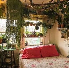 a bedroom with plants hanging from the ceiling and a bed covered in pink pillows,