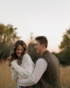 a man and woman standing in the middle of an open field smiling at each other