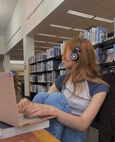 a woman with headphones on sitting in front of a laptop computer at a library