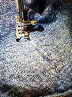 the sewing machine is stitching through some blue jeans with holes in it's fabric