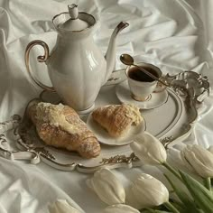 two croissants on a plate next to a tea pot and cup