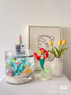 the little mermaid figurine is next to a vase with tulips in it