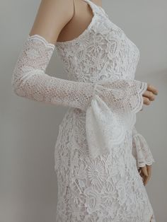 a mannequin wearing a white lace dress with long sleeves and an open shoulder