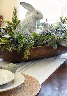 a wooden bowl filled with plants and two white rabbits