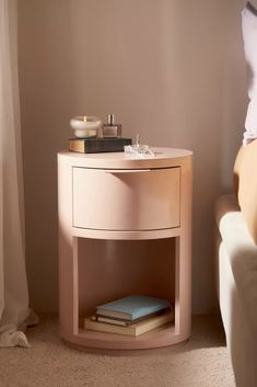 a nightstand with books on it next to a white couch in a room that has light colored walls