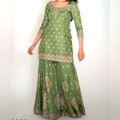 This Earth Toned Green Ananda Suit With Cream And Pink Floral Thread Work Brings Simplicity And Tradition Together. The Lightweight Fabric Brings Ultimate Comfort For Your Daytime Events. Finished With Piping, The Blouse Also Has Closely Stitched Floral Patterns To Create A Border To Delicately Frame The Top. The Bold Thread Work Designed For The Sharara Pants Adds The Perfect Wow Factor To This Simple And Grounded Look. Both Blouse And Pants Are Lined In Butter-Crepe To Provide Structure And Op Fitted Green Sharara For Spring, Fitted Pista Green Sharara For Spring, Fitted Green Dress With Zari Work, Fitted Pista Green Dress With Mirror Work, Anarkali Tunic Dress With Mirror Work, Fitted Sharara With Mirror Work For Spring, Green Sharara For Spring Party, Elegant Pista Green Dress With Mirror Work, Spring Pista Green Kurta With Mirror Work