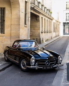 an old black car parked on the side of the road in front of a building