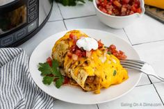 a white plate topped with an enchilada next to a bowl of salsa