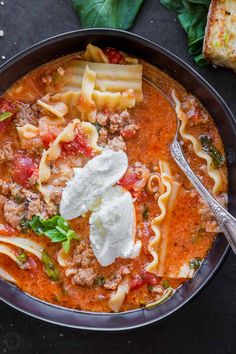 a bowl of pasta soup with meat, cheese and spinach leaves on the side