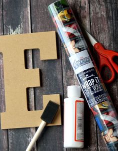 some craft supplies are laying out on a wooden surface with the letter e in the background