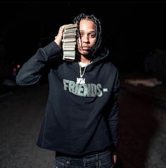 a young man with dreadlocks holding stacks of books over his head in the dark