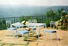 an outdoor table and chairs on a patio overlooking the mountains with flowers in vases