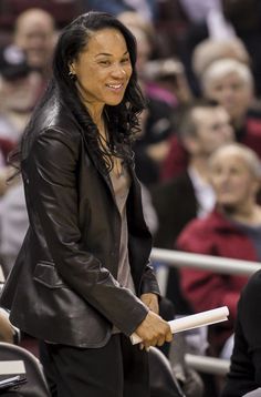 a woman in black jacket and pants standing next to a basketball court with people watching