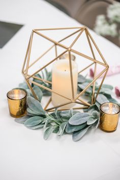 candles and greenery on a white table with gold geometric candle holders in the shape of a hexagonal structure