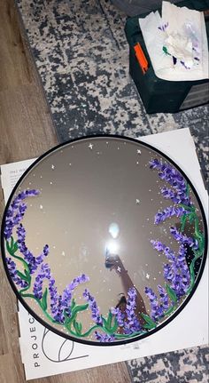 a mirror with purple flowers in it on the floor next to a piece of paper