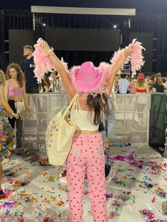 a woman in pink pants and a hat with feathers on her head is standing near confetti