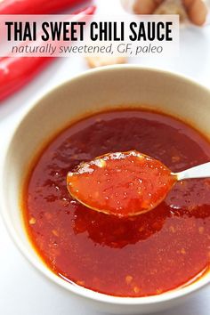 a spoon full of tomato sauce in a white bowl with red chili peppers and garlic on the side