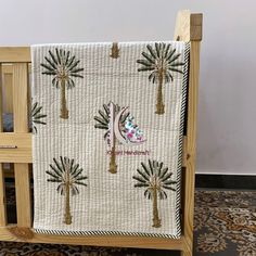 a baby crib with a palm tree quilt hanging from it's front end