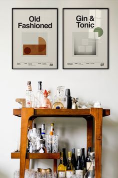 two framed posters above a bar cart filled with bottles and glasses