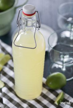 a bottle of lemonade sitting on top of a table next to glasses and limes