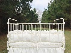 a white crib in the middle of a field with trees and grass behind it