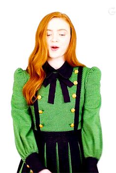 a woman with long red hair wearing a green and black dress standing in front of a white background