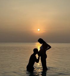 two people are standing in the water at sunset, one is touching the other's chest