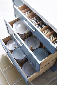 an open cabinet filled with dishes and plates on top of a tiled floor next to a counter