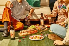 two people sitting on the floor with food and wine