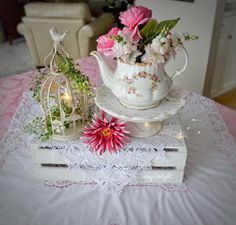 a white tea pot sitting on top of a table next to a vase filled with flowers