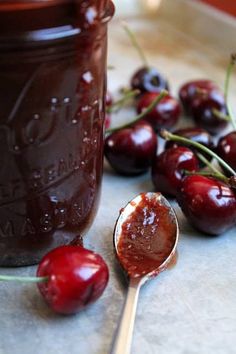 a spoon with some cherries on it next to a jar of jam