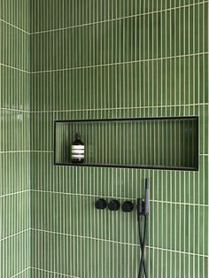 a green tiled bathroom with a shower head and soap dispenser on the wall