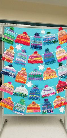 a bulletin board with knitted hats hanging from it's sides and snowflakes on the top