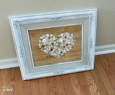 a white frame with a heart made out of buttons on the floor next to a wall