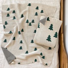 a blanket with green trees on it sitting on top of a wooden bed next to a pillow