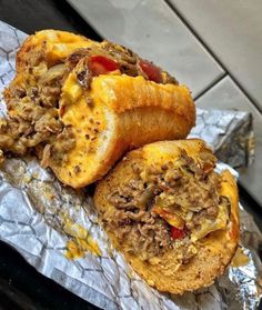 two pieces of bread with meat and cheese on it sitting on aluminum foil next to a tile floor