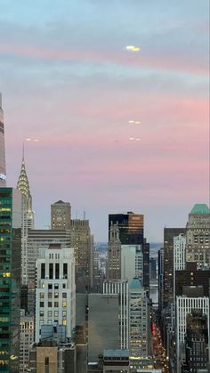 the city skyline is lit up at dusk with skyscrapers in the foreground and pink clouds in the sky