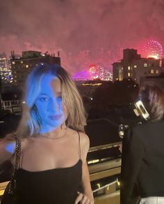 two women are standing on a balcony with fireworks in the background