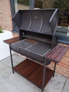 an outdoor bbq grill sitting on top of a wooden table next to a brick building