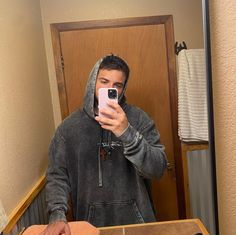 a man taking a selfie in front of a mirror while wearing a hoodie