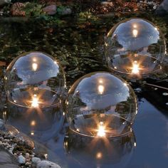 three glass balls sitting on top of a pond filled with water and lit by lights